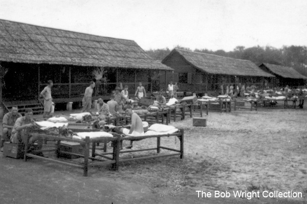 Signals Huts
Birdwood Camp, Singapore, 1941.

"This snap shows the two huts belonging to the Sigs, on the Sunday morning clean up. Seated on the charpoy in the foreground is Bill Moncrieff, one of the Wagga lads. Standing at the back with hands on hips is "Hank" Massey. George Coote is fellow with the "high forehead", Laury Quintal, who traces back to Fletcher Christian of the Mutiny of the Bounty is sitting down a little in front of George.

I'm over in the other hut, of which there will be a further snap soon."

1) NX53639 - DAVIDSON, Ernest Leslie (Les), Pte. - HQ Company, Signals Platoon (seated left back)
2) NX36759 - MONCRIEFF, William Henry (Gladys), Pte. - HQ Coy. Sig. Pl. to 8 Div. Sigs. 10/11/1941, Doi Malaya Hamlet (Pellagra, Dys) (seated on charpoy at front)
3) NX25715 - MASSEY, Thomas Fox (Hank), L/Cpl. - HQ Coy. Sig. Pl. (standing left back with hands on hips)
4) NX47129 - COOTE, George Bentley, Pte. - HQ Coy. Sig. Pl. Doi Sonkurai 1 (Cholera)
5) NX65486 - QUINTAL, Laurie Patterson, Pte. - HQ Coy. Sig. Pl. Doi Tanbaya (Beri Beri, Dysentery) (sitting on charpoy in background)
6) NX36166 - WRIGHT, Robert, Cpl. - HQ Coy. Sig. Pl.

1. The photographs are to be known as The Bob Wright Collection.
2. Reproduction of the Collection or any part of it is prohibited without written permission.
3. Permission is granted to the 2/30th Batallion Association to reproduce the Collection as it deems appropriate.
4. Permission is granted to the Australian War Memorial Museum to reproduce the Collection as it deems appropriate.
5. All other permission is specifically withheld.
6. Written application for permission to reproduce the Collection, or part of it, may be made to:
Mr I. Wright
95 Hewitt Avenue
Wahroonga 2076 New South Wales

